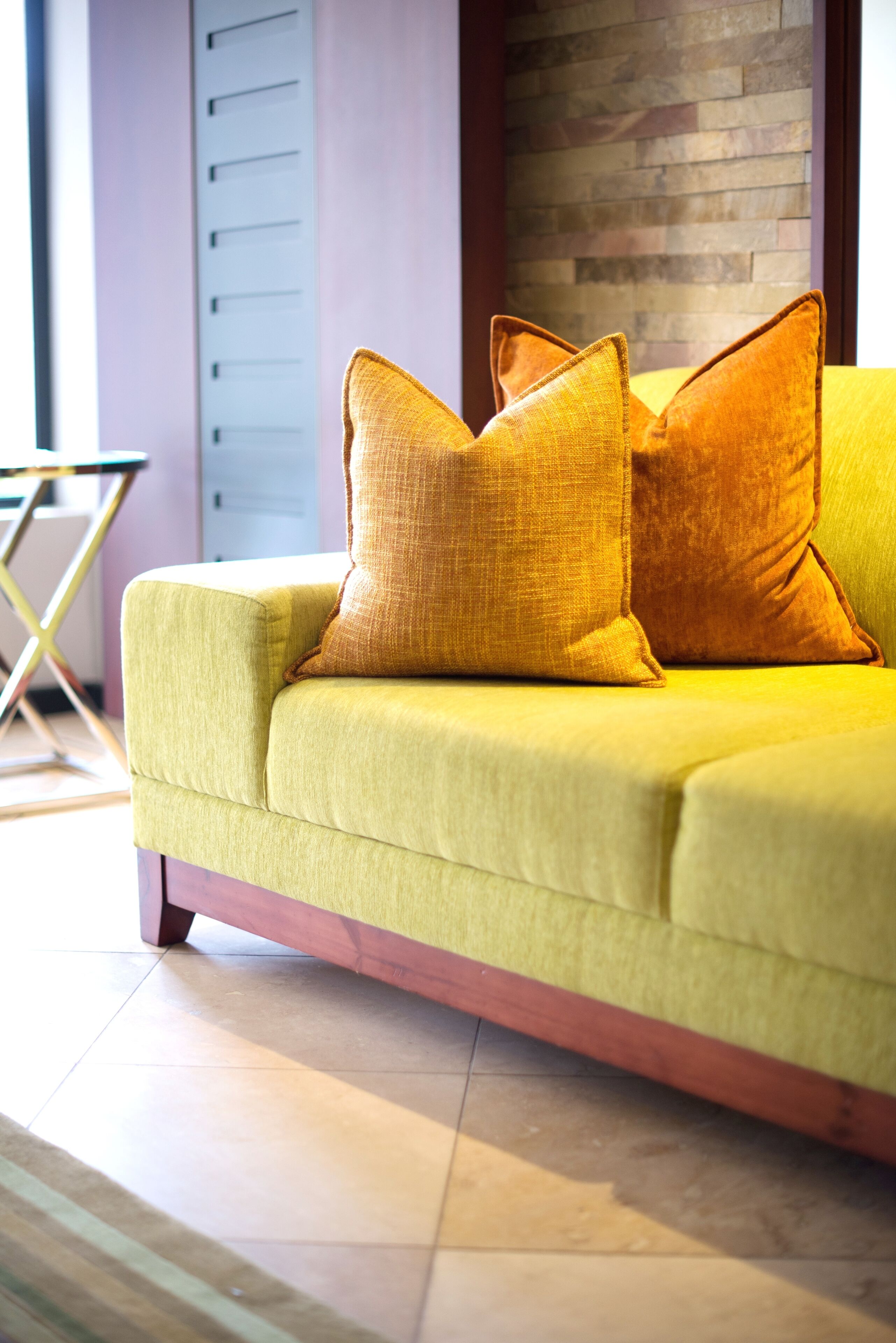 A yellow sofa with two cushions, a wooden floor, and a brick wall in the background.