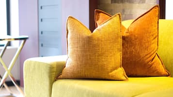 Um sofá amarelo com duas almofadas, piso de madeira e parede de tijolos ao fundo.