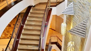Ein mehrgeschossiges Interieur mit einer zentralen Treppe, einer Rezeption und dekorativer Beleuchtung.