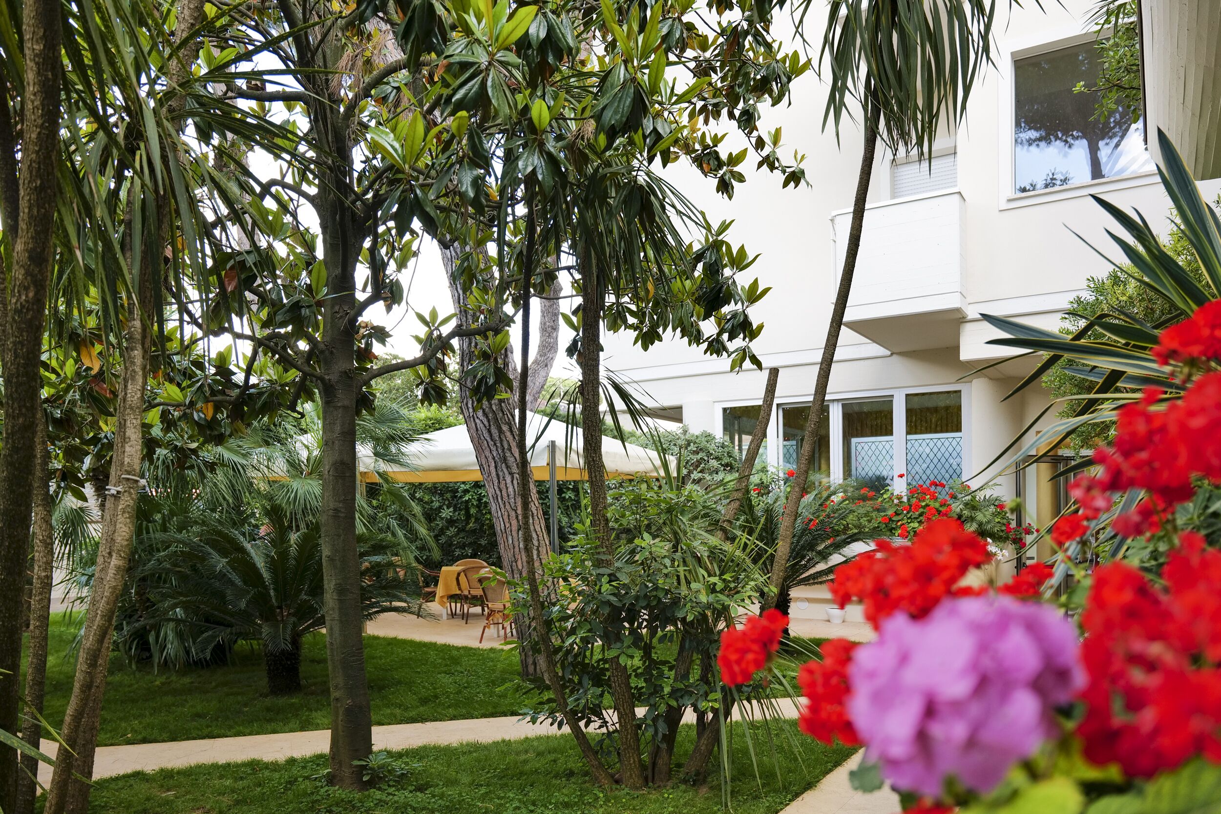 Un edificio moderno con un jardín bien cuidado, que incluye palmeras y plantas con flores.