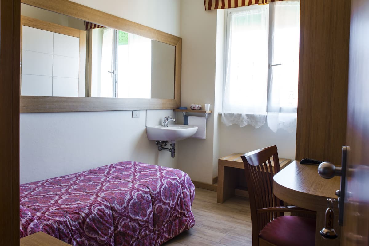 A bedroom with a bed, a bedside table, a chair, a sink, and a window with curtains.