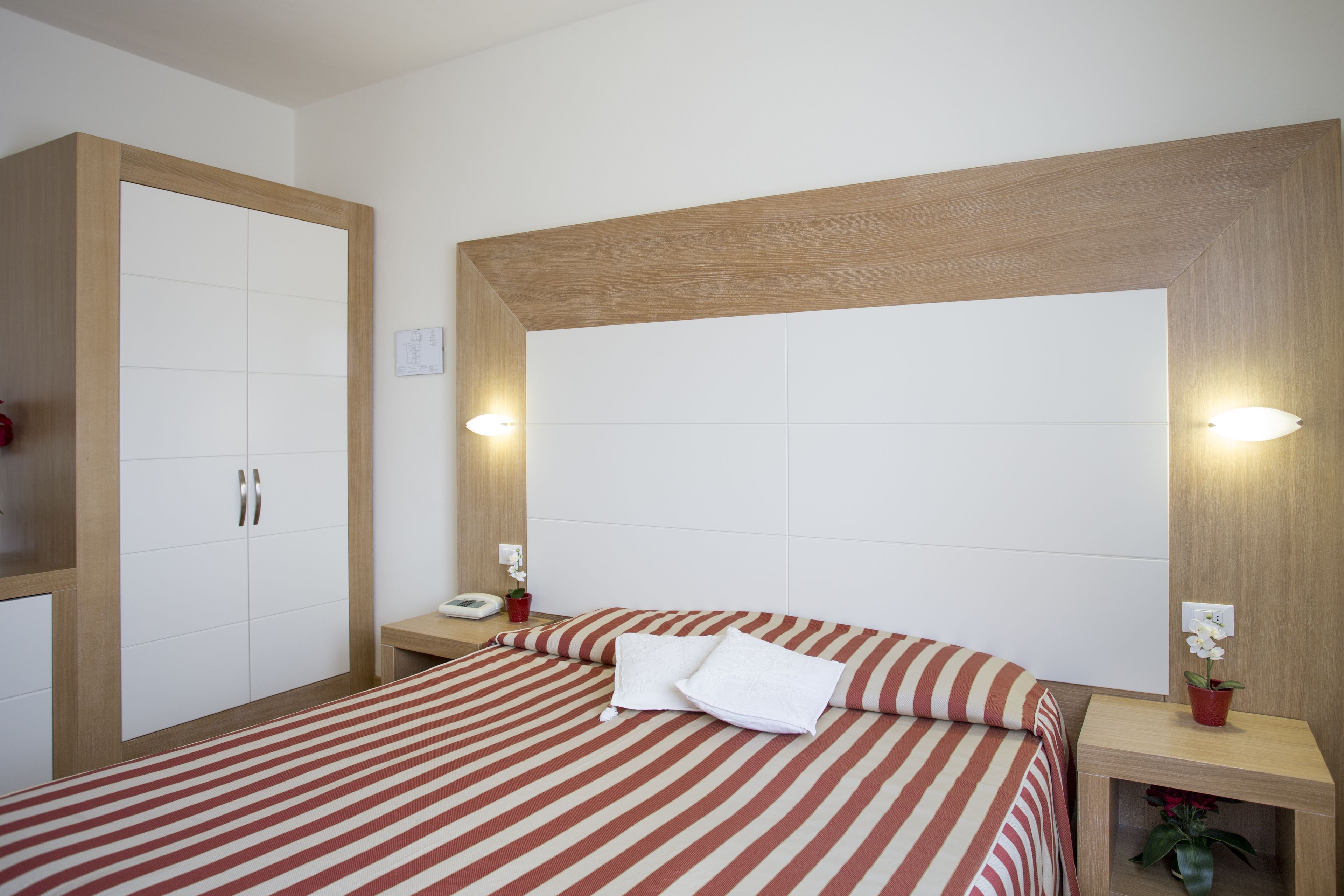 Habitación de hotel con una cama grande, un armario, mesitas de noche y una mesita auxiliar con una planta.