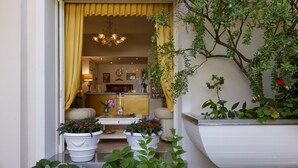 A well-lit entrance with a yellow curtain, a chandelier, and potted plants. - Hotel Sylvia (Camaiore)