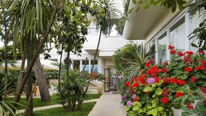 A pathway leading to a building with a glass door, surrounded by lush greenery and flowering plants. - Hotel Sylvia (Camaiore)