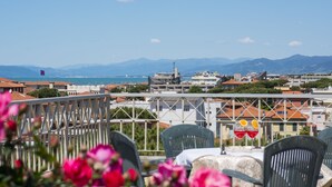 A terrace with a table and chairs, overlooking a coastal cityscape with mountains in the distance. - Hotel Sylvia (Camaiore)
