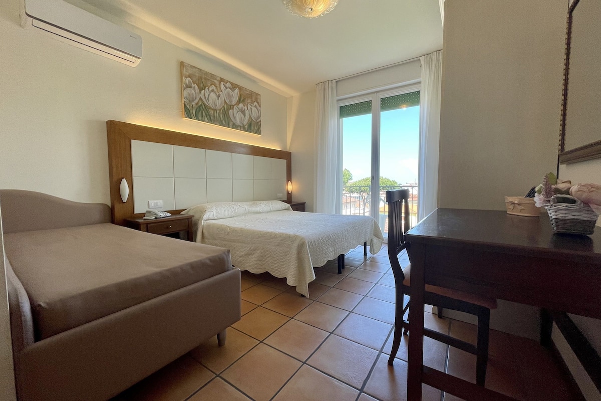 A hotel room with two beds, a desk, and a chair. There is a window with a view of the outdoors.