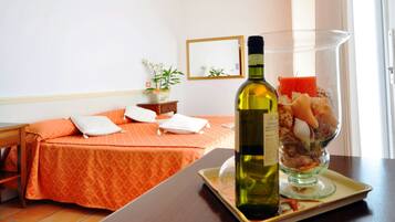 Une chambre d’hôtel avec un lit, une table de chevet, une bouteille de vin et un panier de fruits.