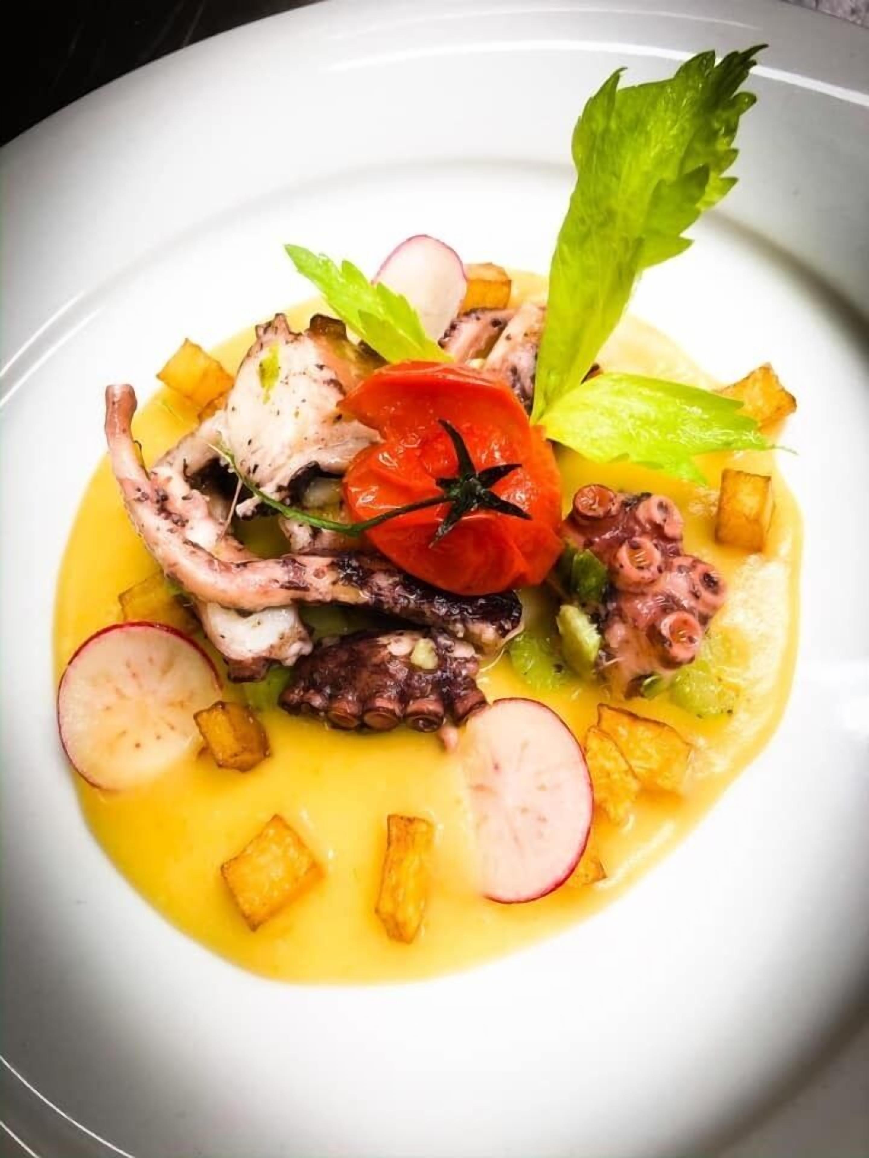 A plate of food with octopus, radishes, and a tomato on a white plate.