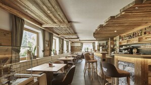 Un restaurante con vigas de madera en el techo, una zona de bar con estantes llenos de botellas y una barra larga. Se han dispuesto mesas y sillas para comer.