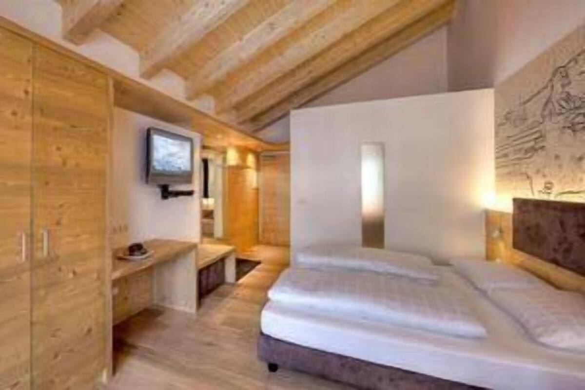 A bedroom with wooden flooring, a bed, a TV, and a desk.