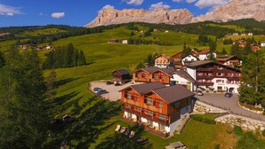 Un pueblo de montaña con casas de madera tradicionales, un edificio central con balcón, y vistas a las colinas y montañas circundantes.