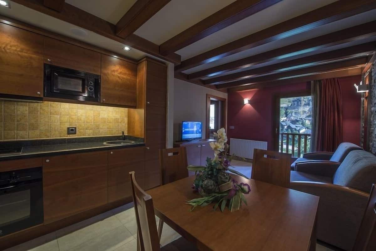 A modern kitchen with wooden cabinets, a built-in microwave, and a dining area with a table and chairs.