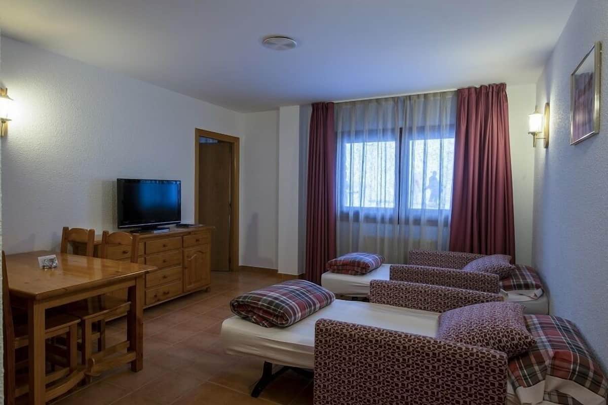 A room with a wooden dining table, a television, and a sofa area with patterned cushions.