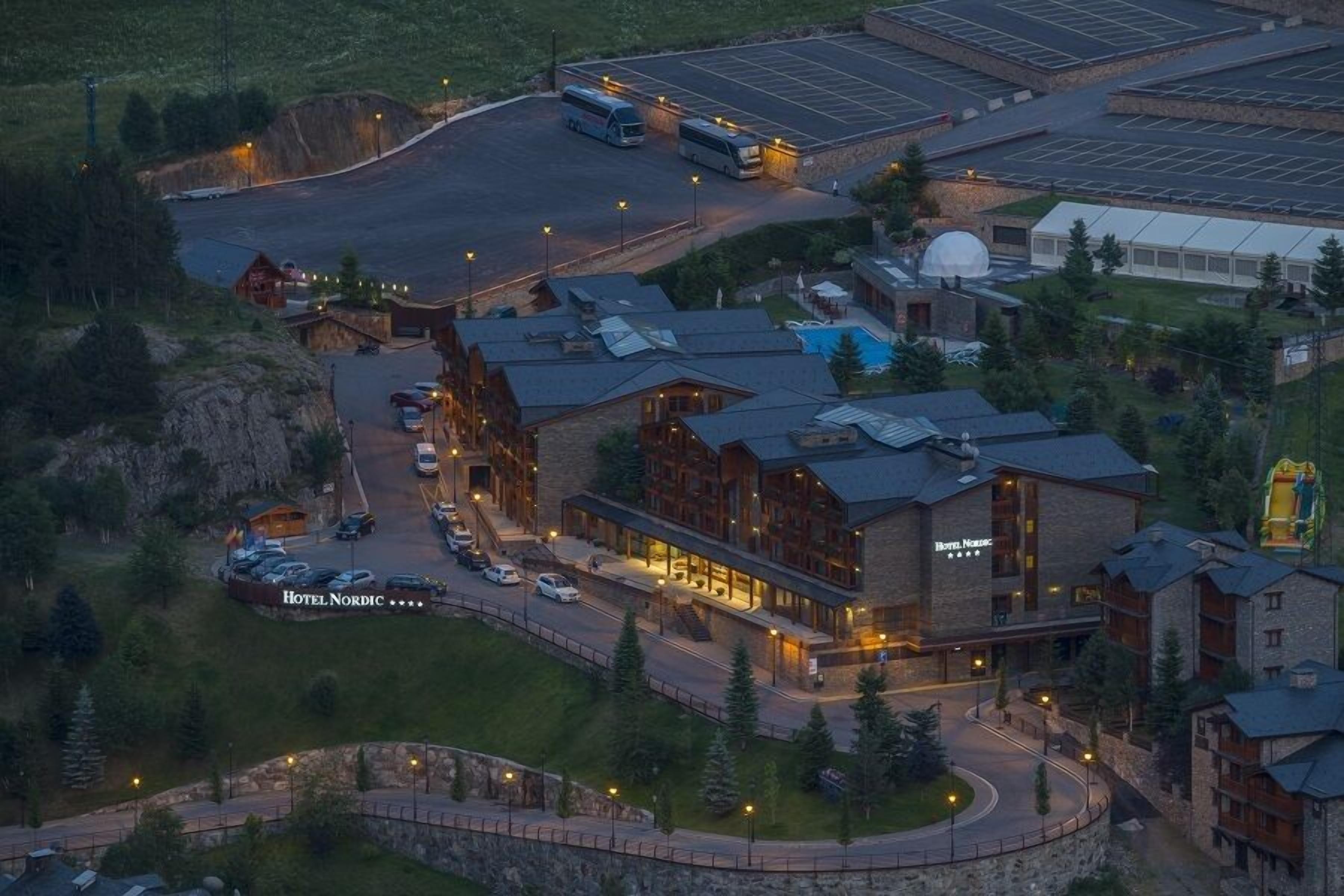 A hotel with a central building, a parking lot, and a greenhouse.