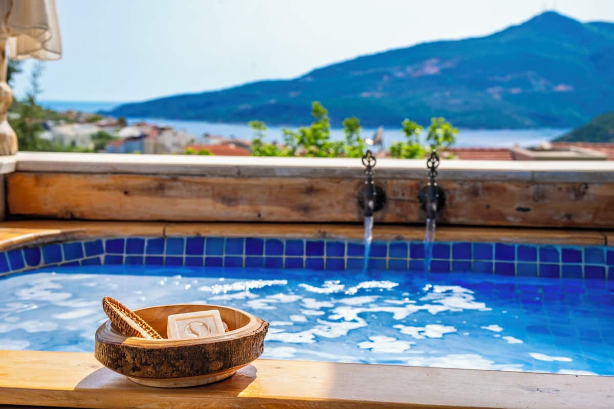 A wooden bench with a bowl containing a candle and a card by a pool with a mountain view.