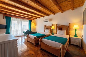 Habitación de hotel con pisos de madera, dos camas con cubrecamas verdes, cabeceros de madera y lámparas de noche.