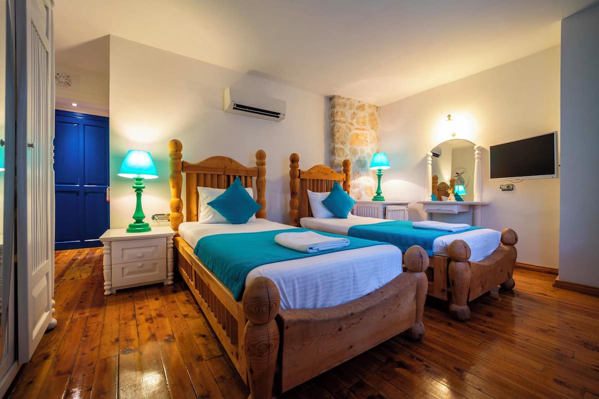 A bedroom with two wooden beds, nightstands, a stone wall, a mirror, and a television.