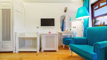 Una habitación con una cama blanca, un sofá azul, un televisor y una mesita de noche con una lámpara.