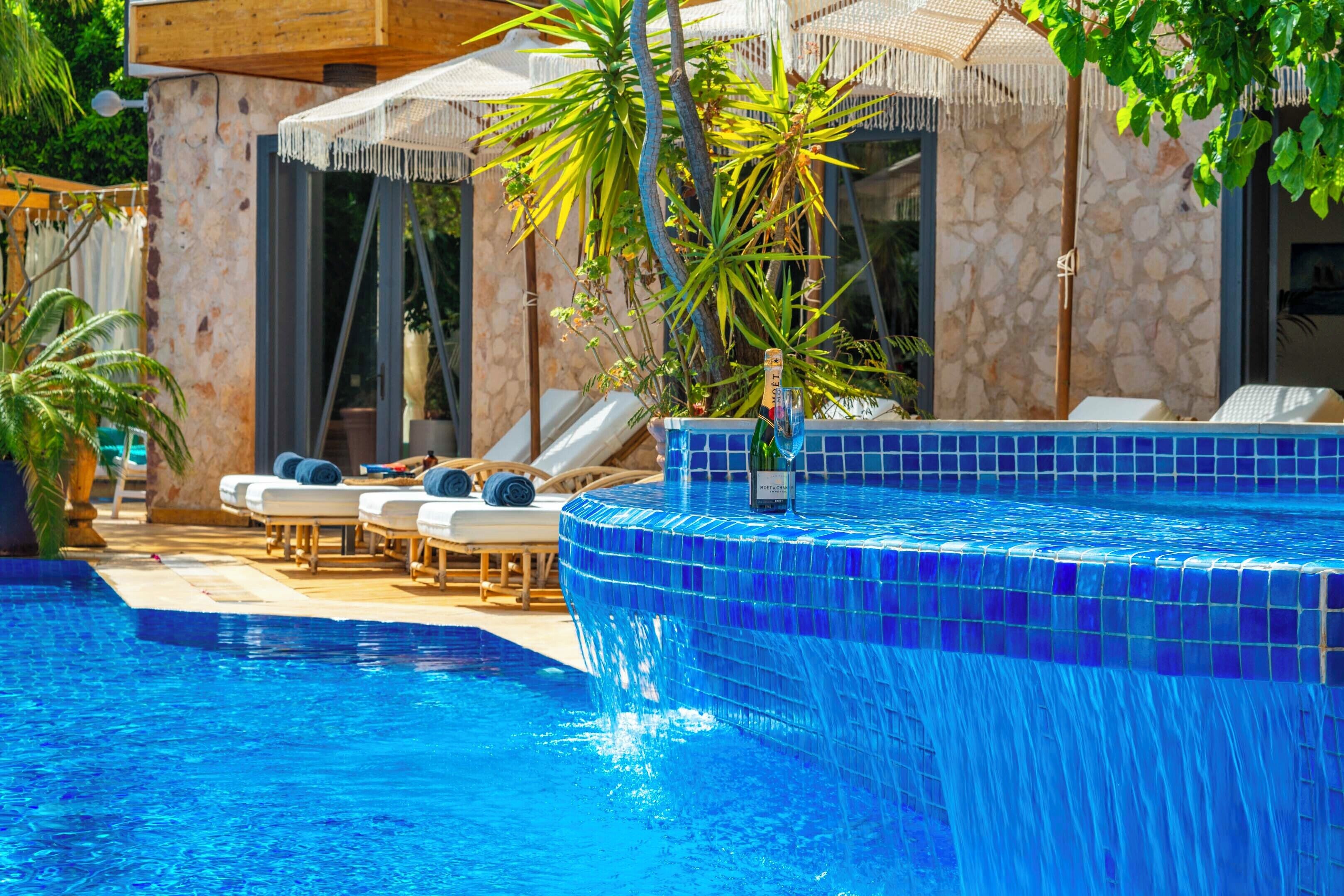 Una piscina con baldosas de mosaico azul, sillas de descanso y sombrillas.