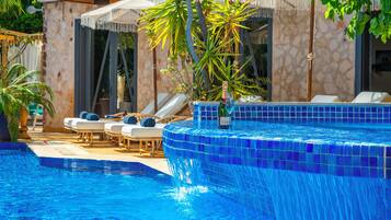 Una piscina con baldosas de mosaico azul, sillas de descanso y sombrillas.