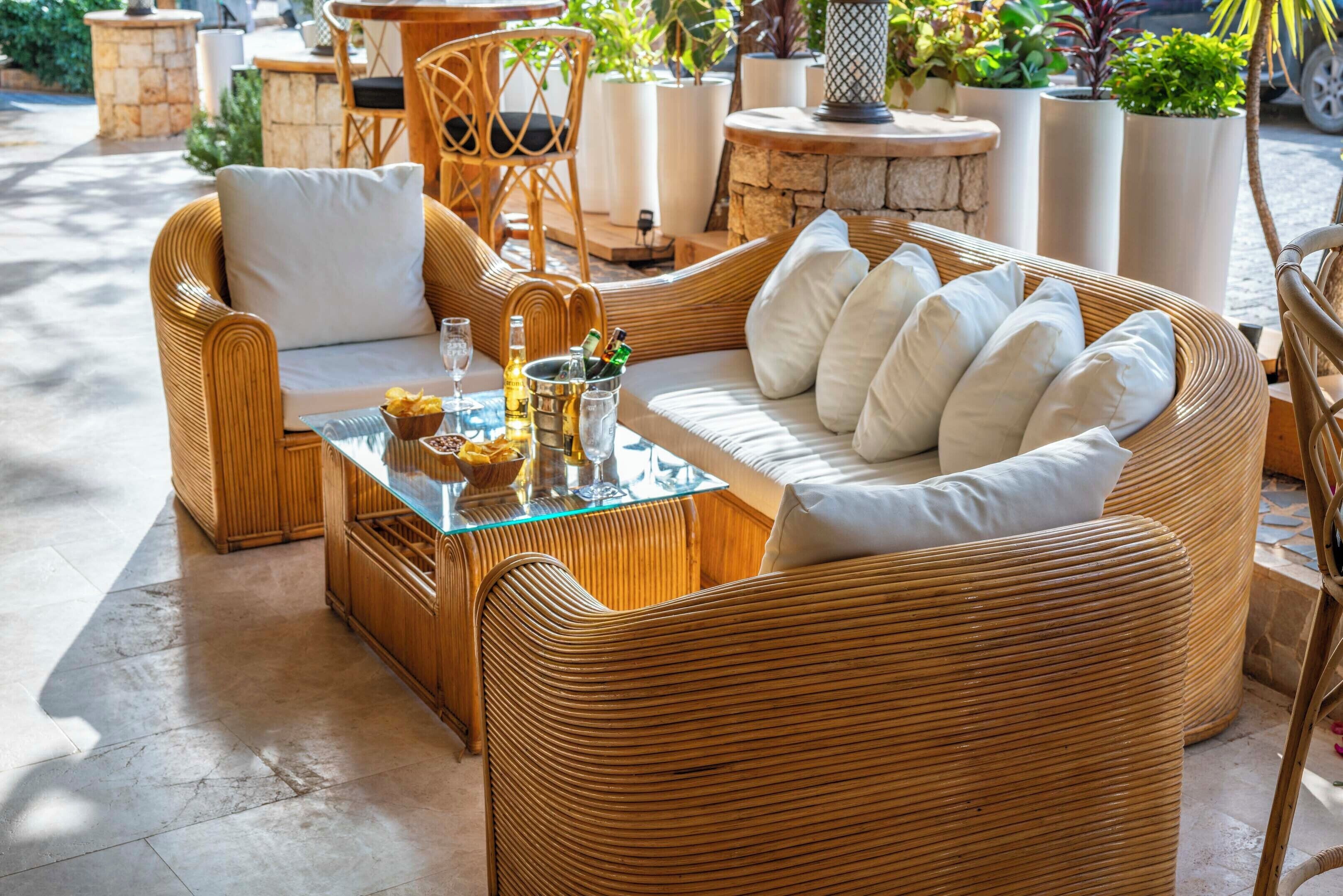 A wicker sofa with white cushions, a glass coffee table with bottles and glasses, and a stone accent wall.