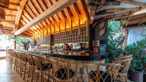 A bar area with wooden ceiling beams, wicker bar stools, and a stone counter. - Elixir Boutique Hotel (Kalkan)