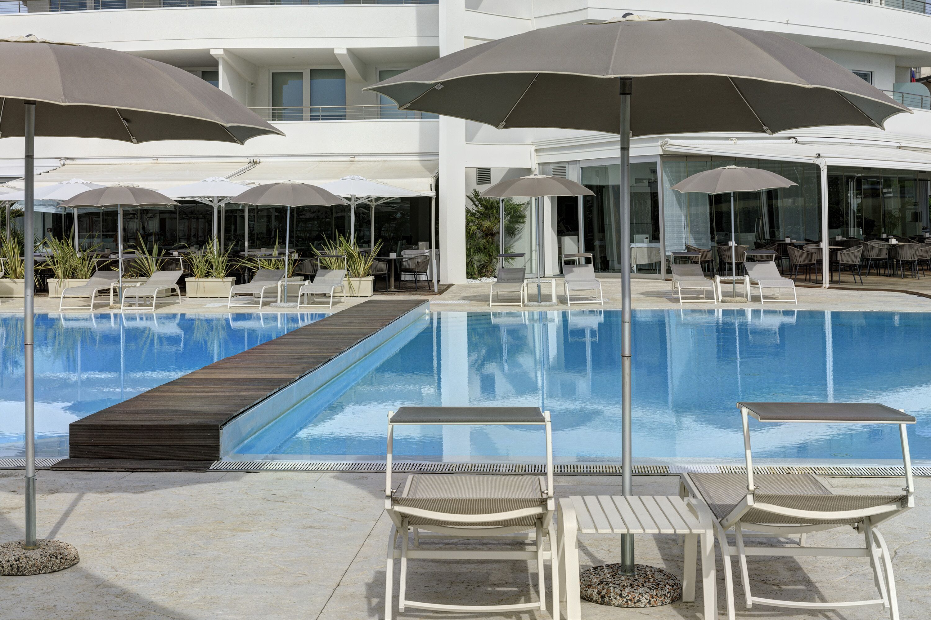 A poolside area with lounge chairs, umbrellas, and a wooden deck leading to the pool.