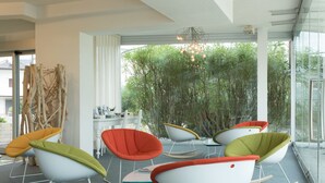 A modern interior with white rocking chairs and a glass wall offering a view of greenery. - Adriatic Palace Hotel (Jesolo)