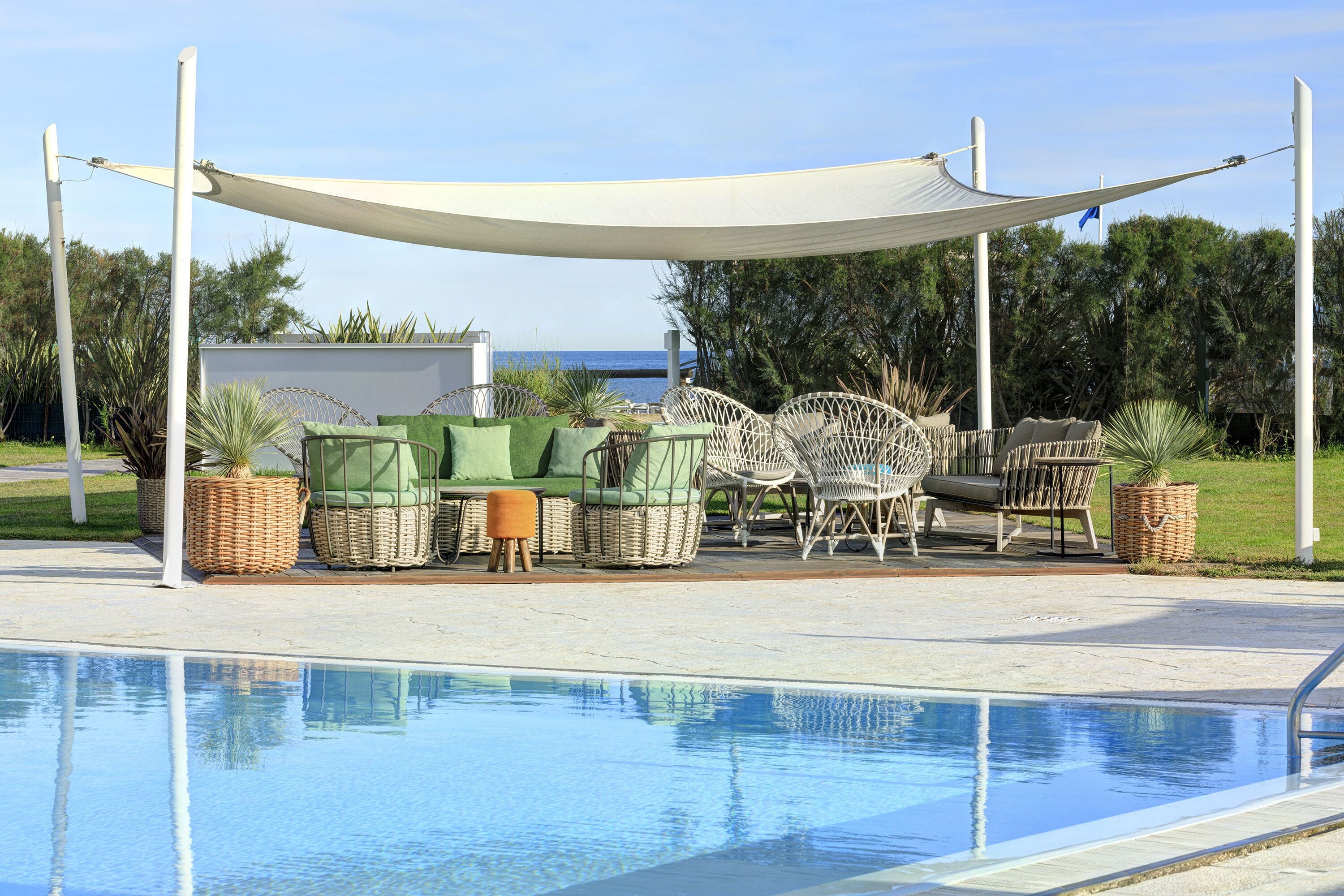 A poolside area with a canopy, wicker furniture, and a view of the sea.