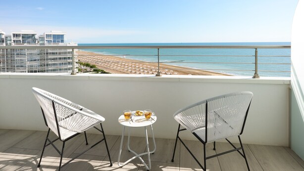 A balcony with two white wicker chairs and a small round table with drinks, overlooking a beach and ocean. - Adriatic Palace Hotel (Jesolo)