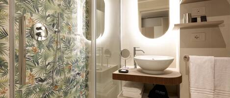 A bathroom with a glass shower enclosure, a white sink with a wooden countertop, and a mirror above the sink.