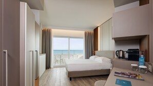 A modern hotel room with a bed, a desk with a coffee maker, a view of the ocean, and a balcony with chairs. - Adriatic Palace Hotel (Jesolo)