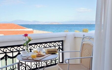 A balcony with a table set for breakfast, a wicker chair, and a view of the sea and mountains.