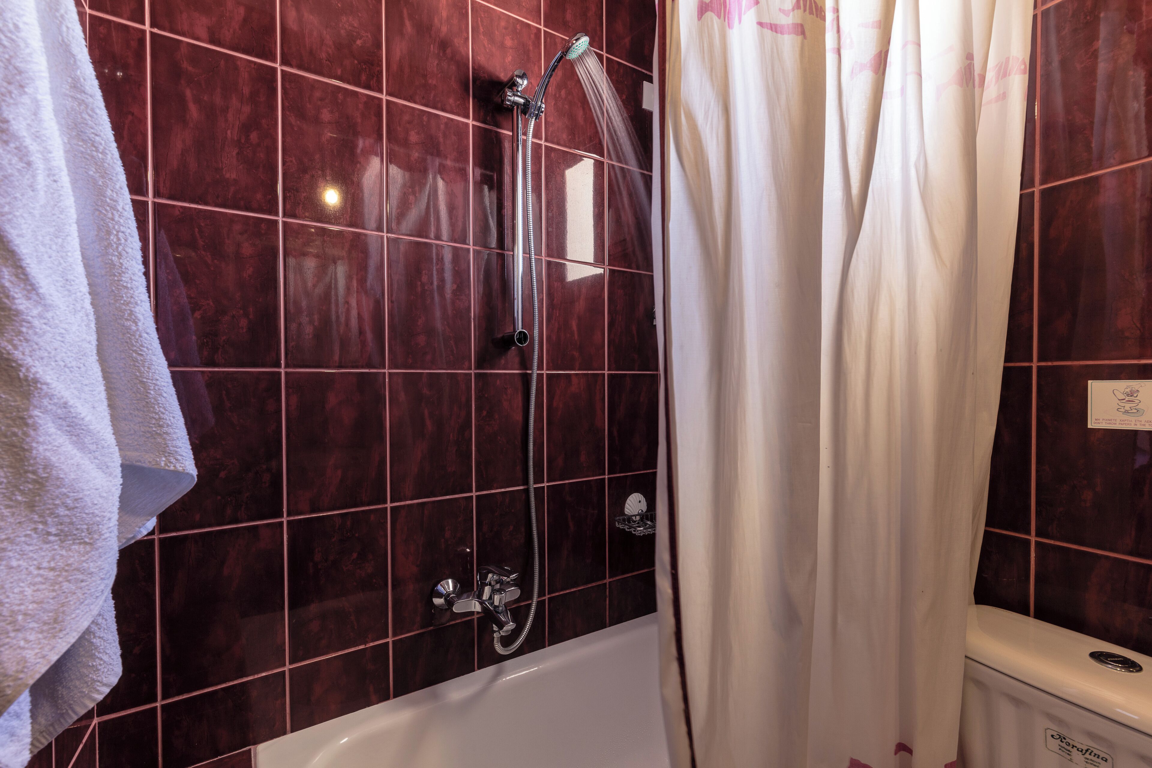 Un baño con una bañera blanca, una ducha con cabezal de ducha manual y una toalla blanca colgada en la pared.