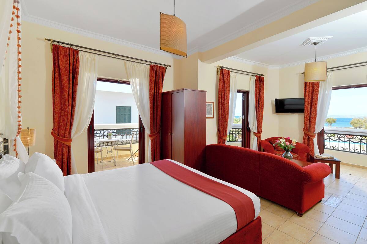 Una habitación de hotel con cama, un sofá rojo, televisión y balcón con vistas.