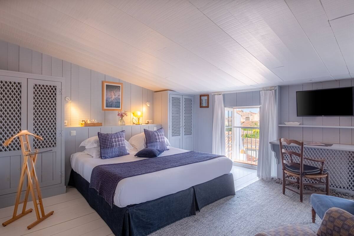 Une chambre avec un grand lit, une chaise en bois, une télévision et un balcon avec vue.