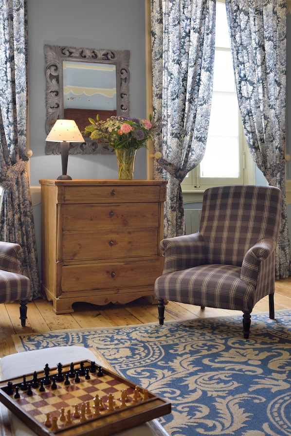 Una habitación con un sillón de cuadros, un aparador de madera y un tablero de ajedrez sobre una alfombra estampada.