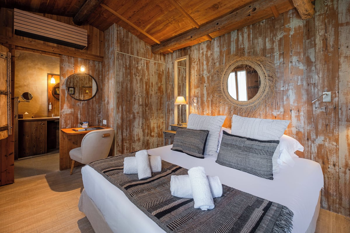 Une chambre de style cabane en bois, avec un grand lit, deux tables de chevet, une chaise et un miroir au mur.