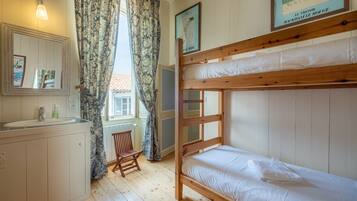 Quarto com uma cama beliche, um armário de madeira com pia, uma cadeira e uma janela com cortinas.