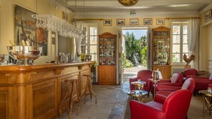 Uma área de bar com balcão de madeira, banquetas e uma grande tigela decorativa. Há cadeiras vermelhas e uma mesa com um copo.
