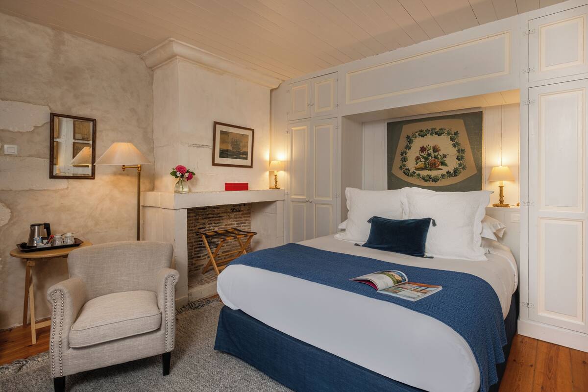 Une chambre à coucher bien rangée, avec un lit, une chaise, une petite table et une cheminée.