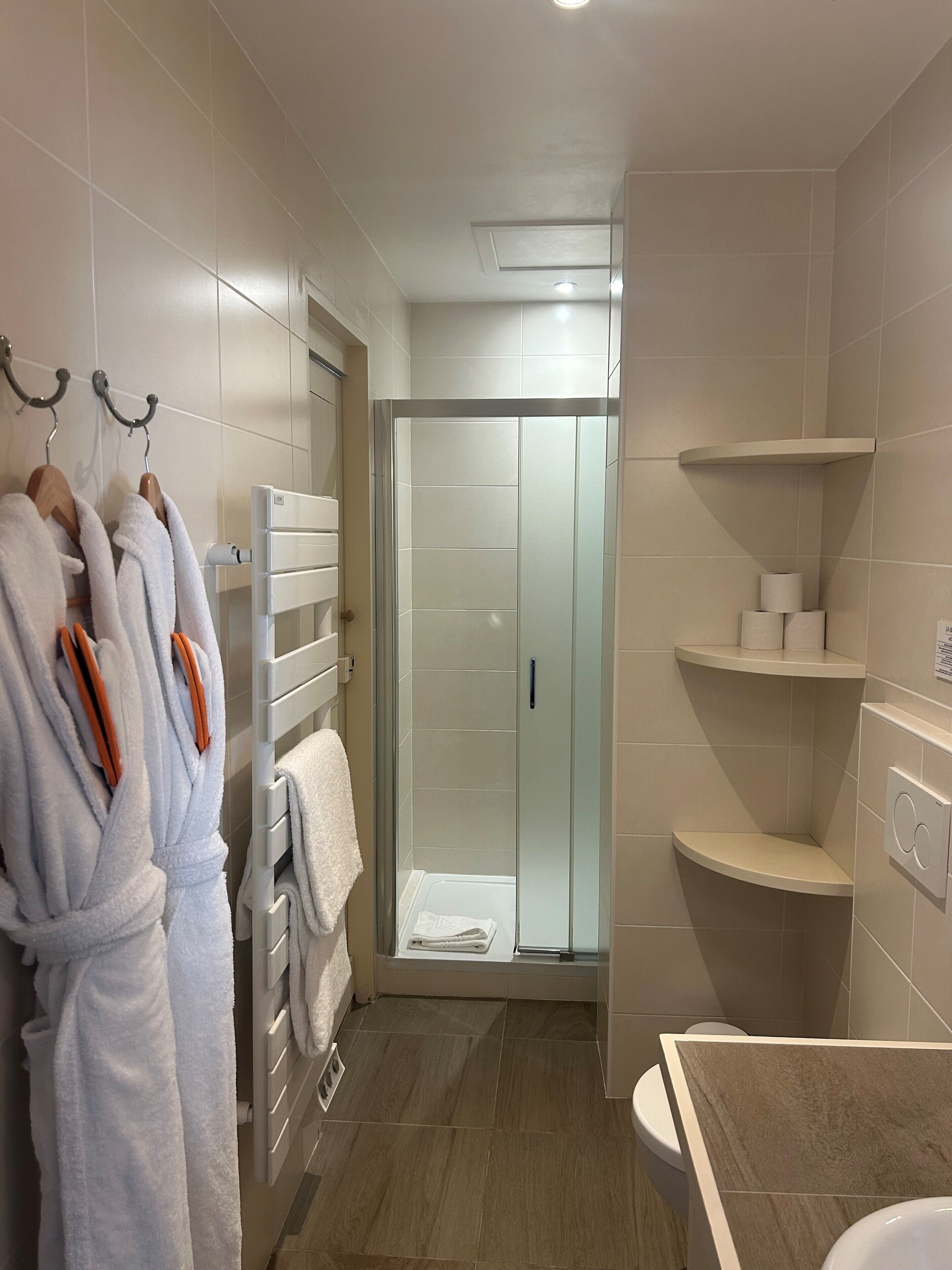 A modern bathroom with a glass shower enclosure, a white bathtub, and a towel rack with robes.