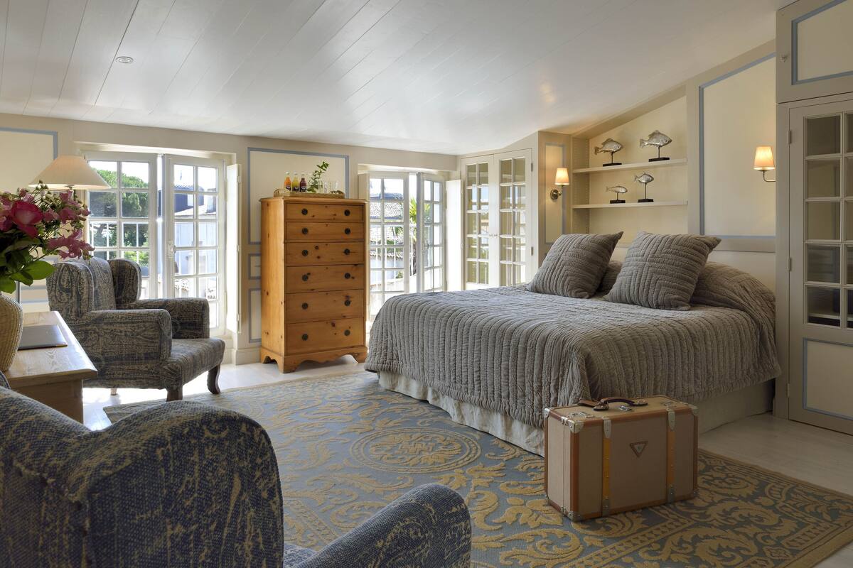 Une chambre avec un grand lit, une commode en bois, un bureau et une chaise. Une valise est posée sur le sol.