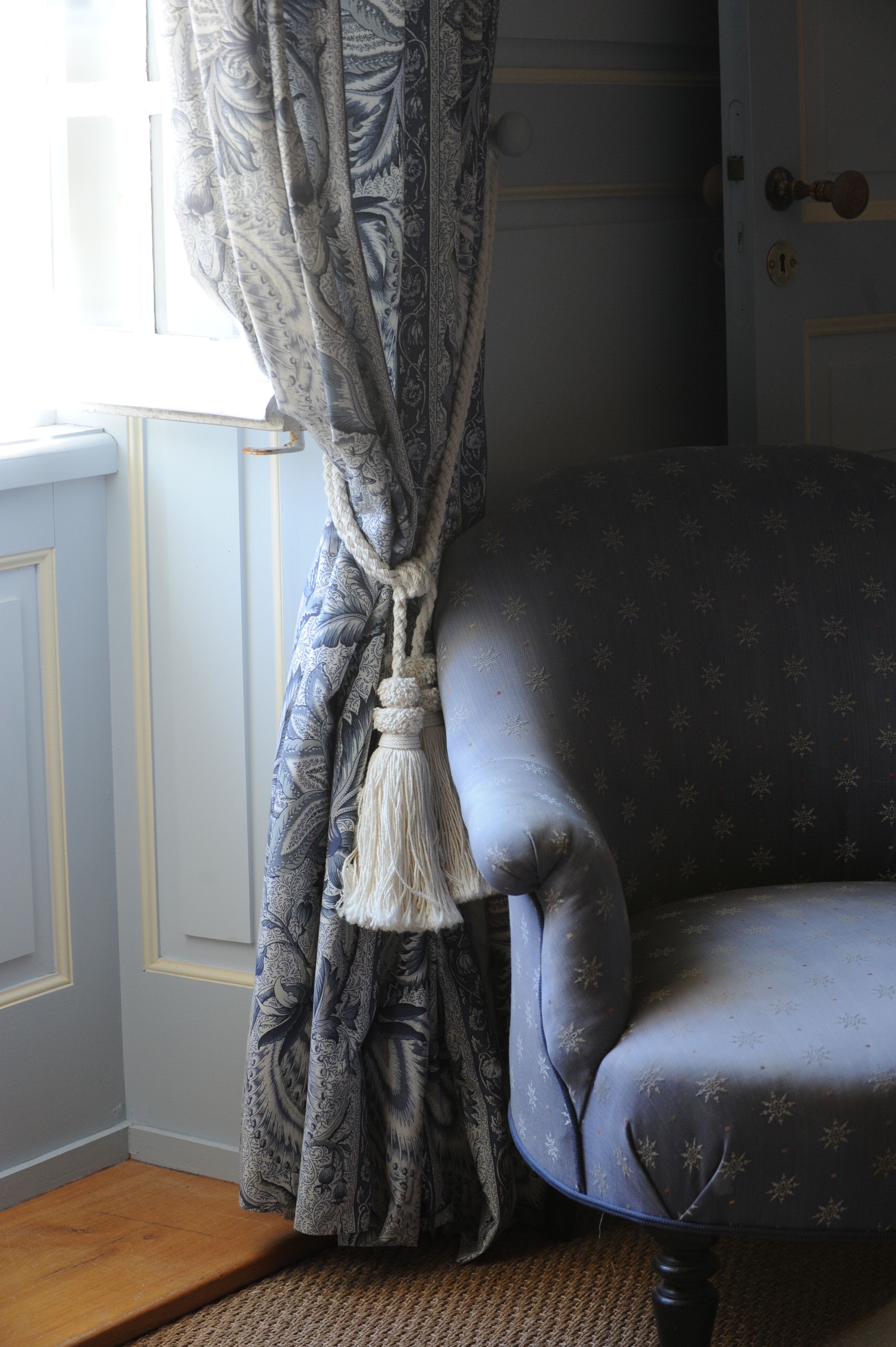 A room with a patterned curtain, a blue armchair, and a wooden floor.