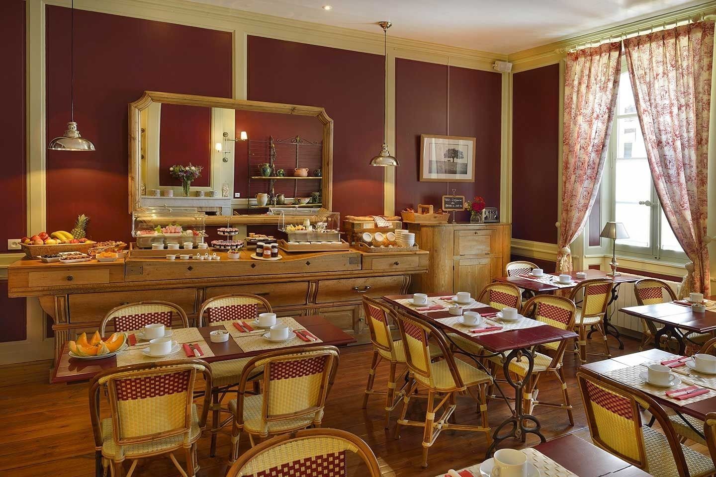 A dining area with wooden tables and wicker chairs, a buffet with various food items, and a large mirror above the buffet.