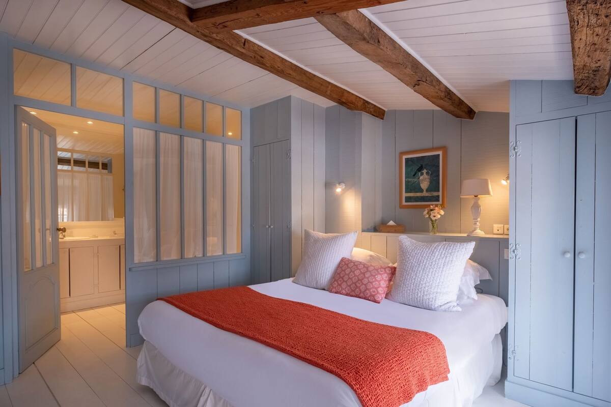Une chambre à coucher avec un lit, une table de chevet, une fenêtre avec des rideaux et une poutre en bois au plafond.