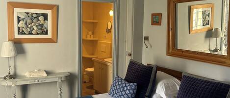 A bedroom with a bed, bedside table, lamp, and a door leading to a bathroom.