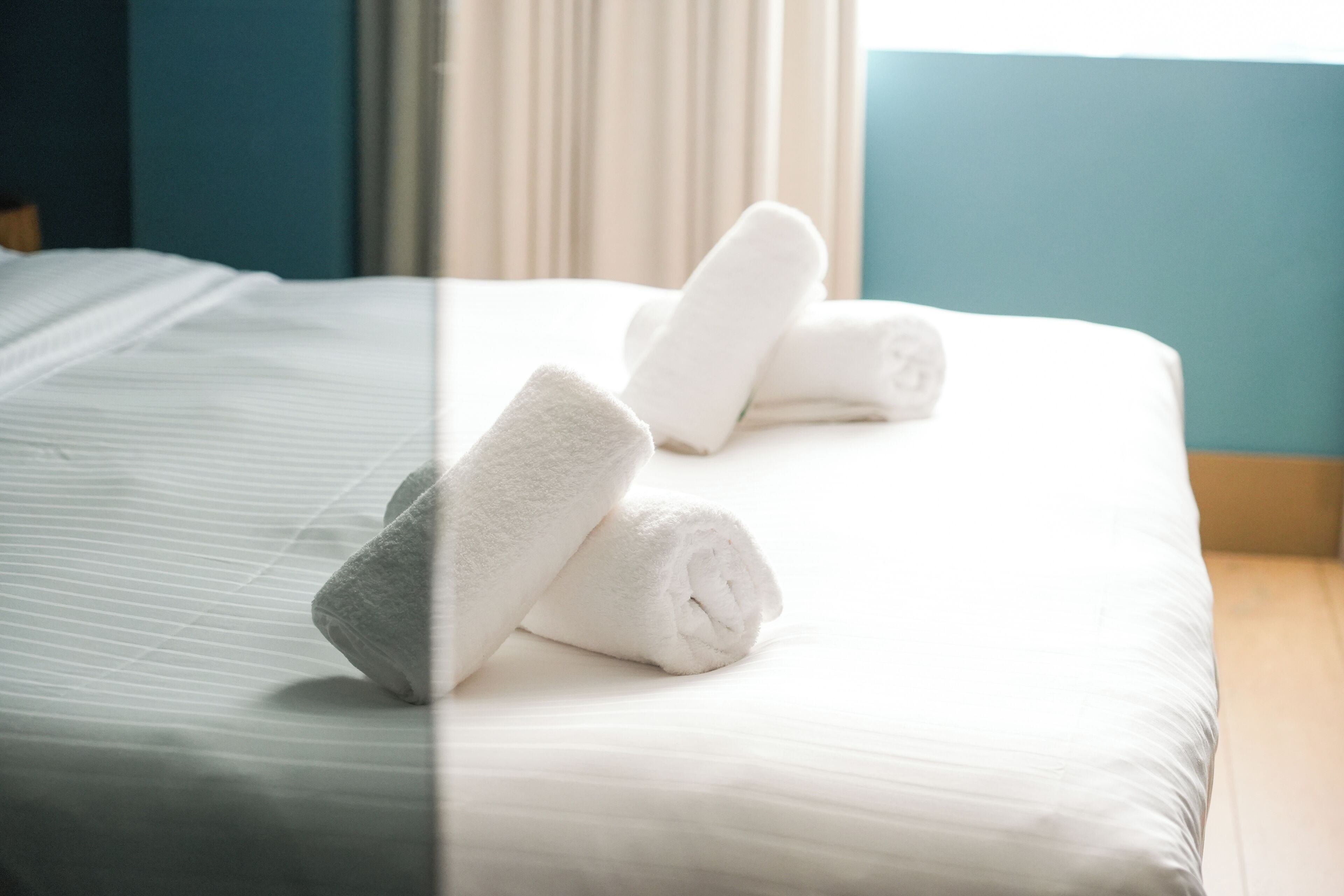 A bed with white linens and rolled towels.