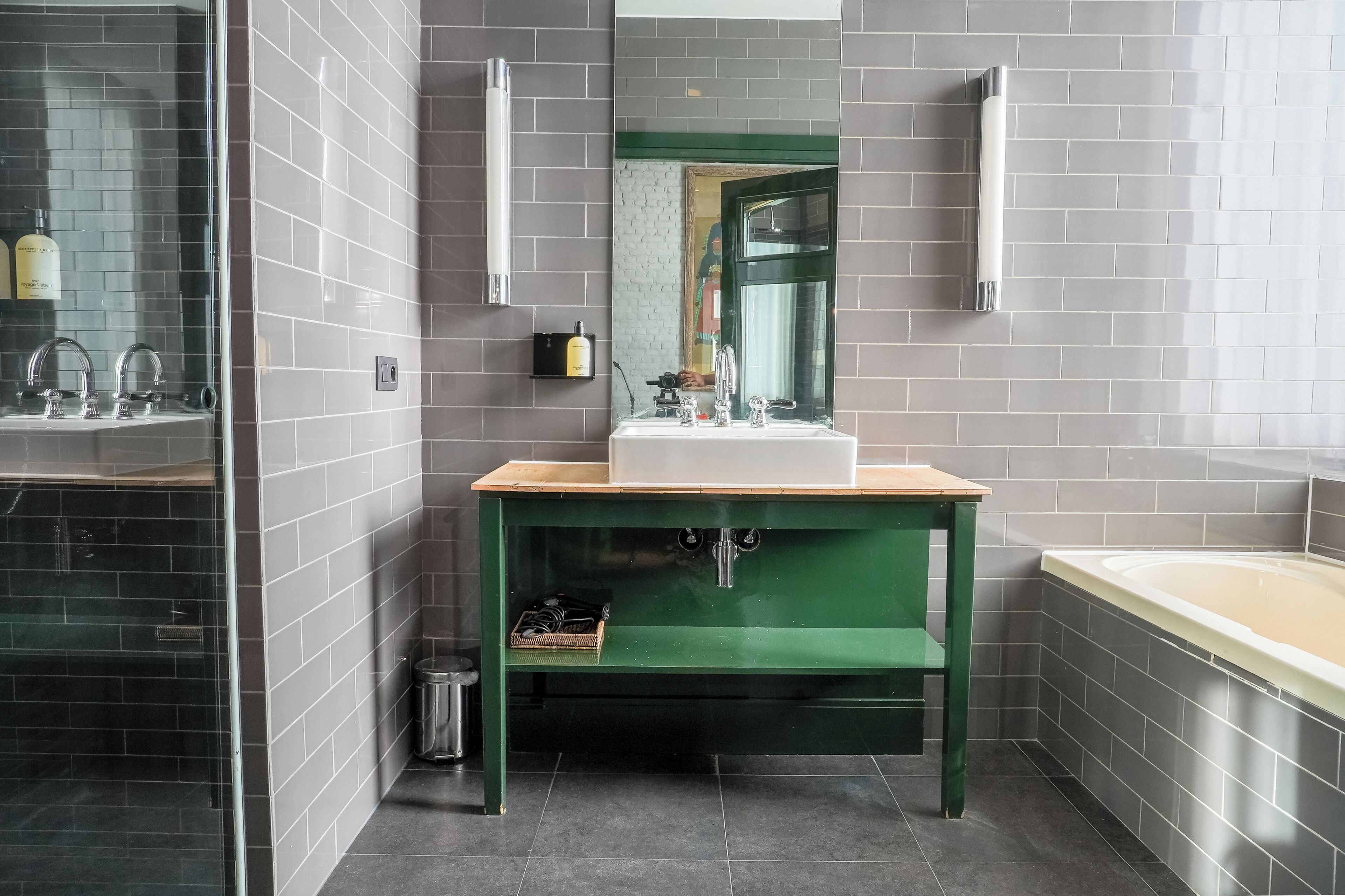 A modern bathroom with a green vanity, a large mirror, and a bathtub.