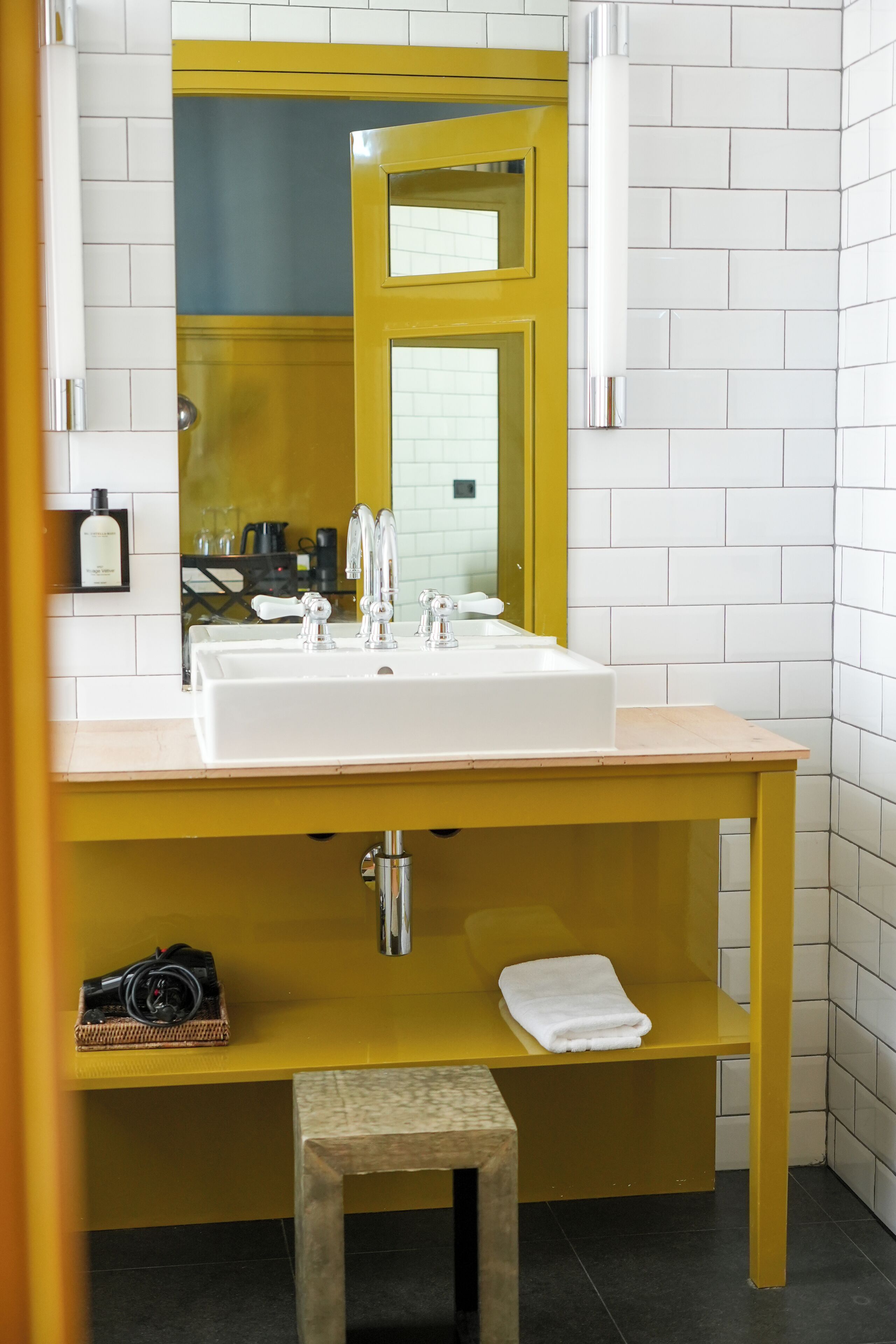 A bathroom with a white sink, yellow vanity, and a mirror.